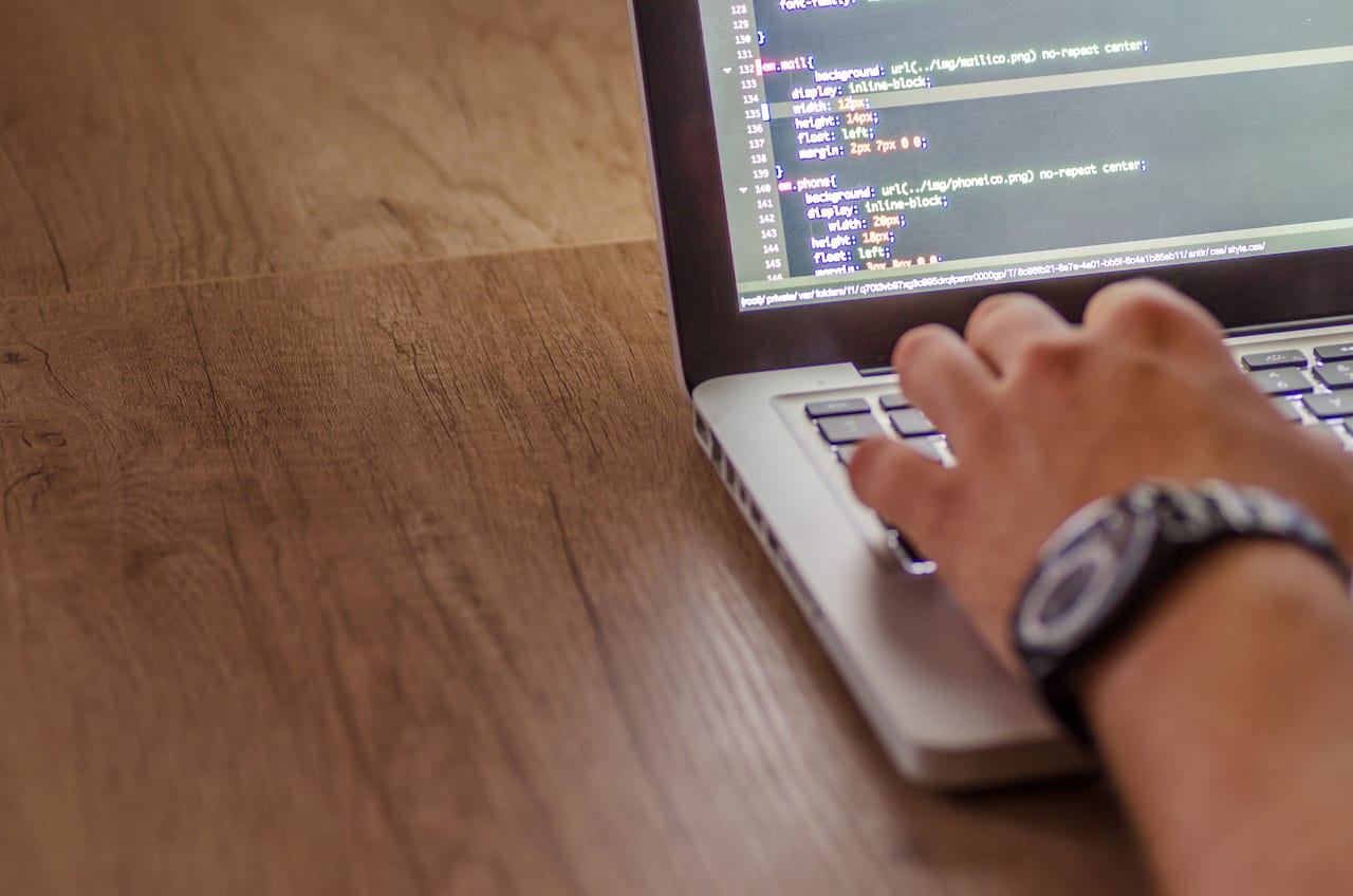 Hand mit Armbanduhr tippt auf einem Notebook, auf dessen Bildschirm CSS-Quelltext steht