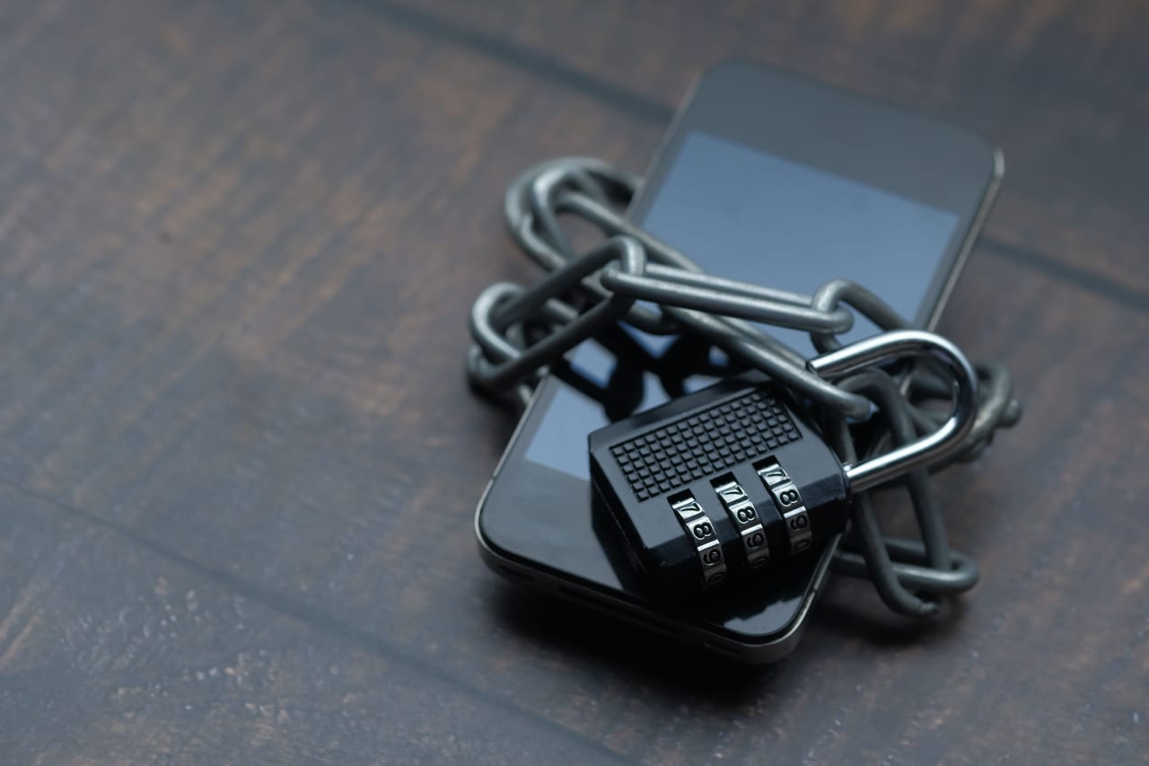 Smartphone, mit einer Metallkette umwickelt und mit einem Zahlenschloss gesichert, auf dunklem Holz
