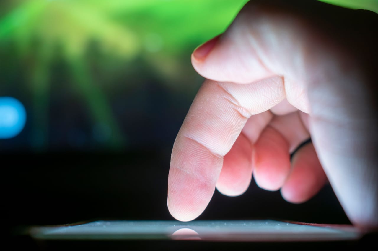 Zeigefinger kurz vor dem Antippen eines leuchtenden Touchscreens, dunkler Hintergrund mit grünem Lichtschein