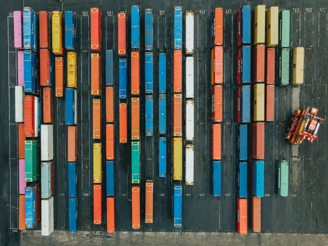 Luftaufnahme eines Containerterminals mit Reihen bunter Frachtcontainer und einem Containerstapler