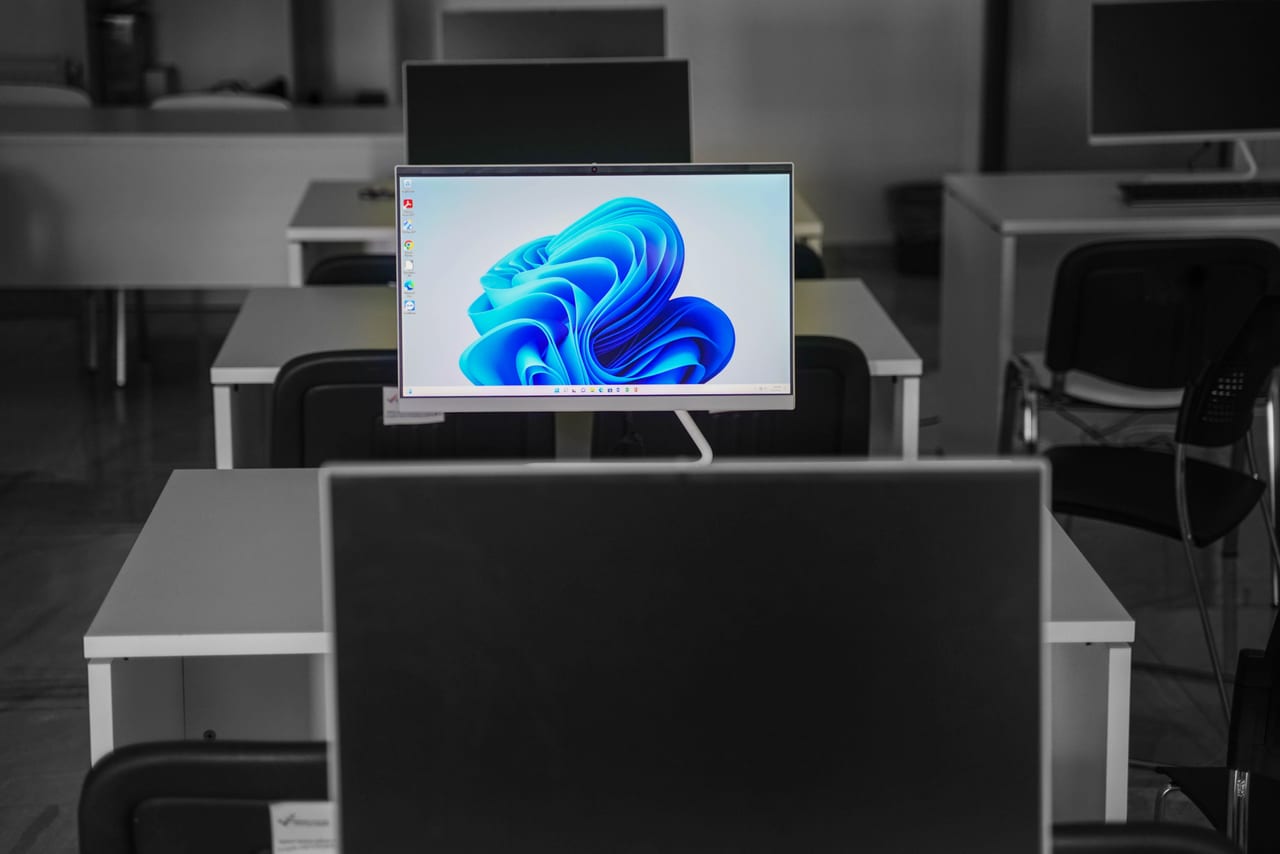 Bildschirm mit Windows-11-Startbild in einem leeren Büro zwischen ausgeschalteten Monitoren