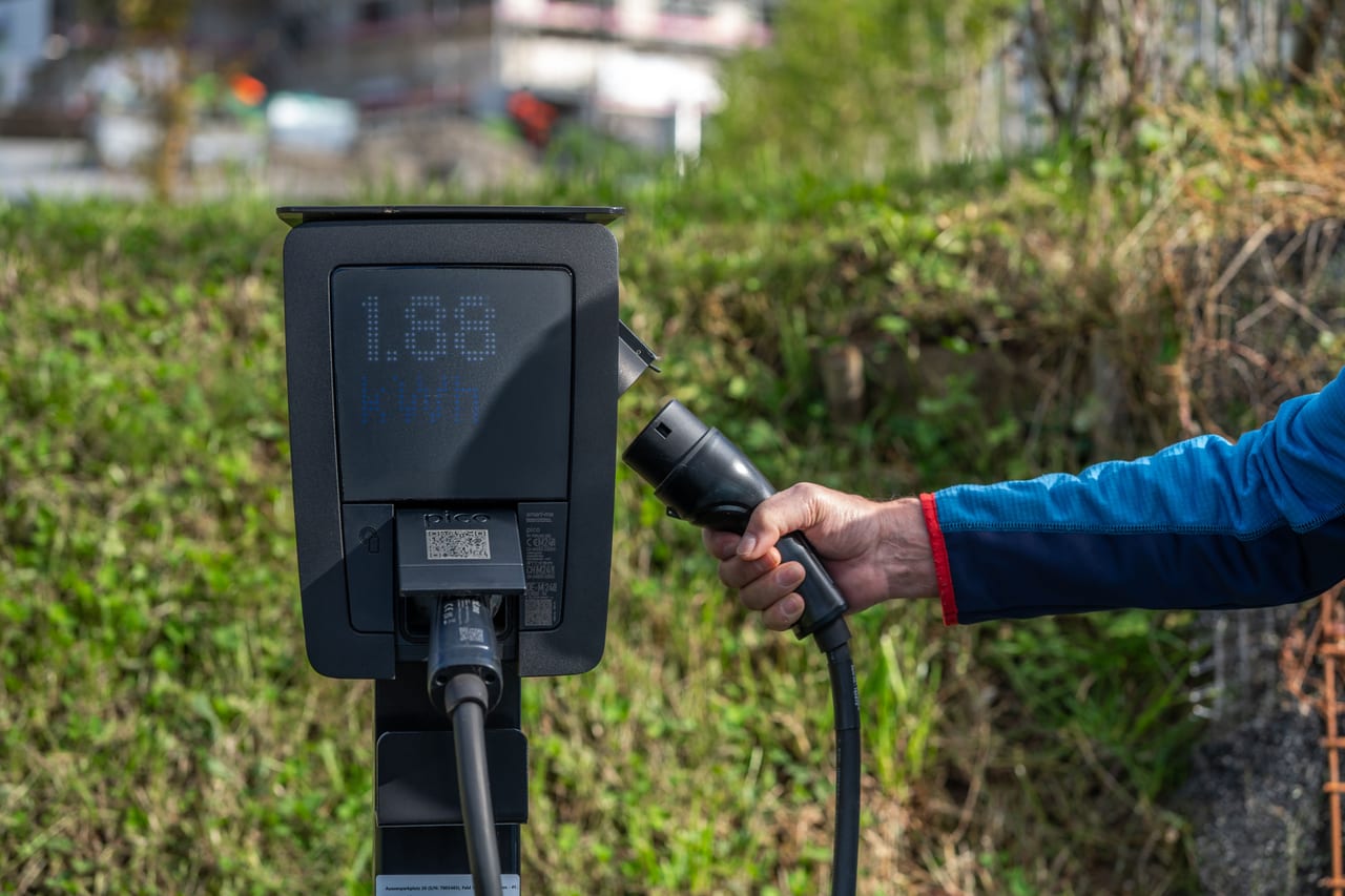 Ladesäule für Elektroautos mit kleinem QR-Code unter dem Display, daneben eine Hand mit dem Ladestecker