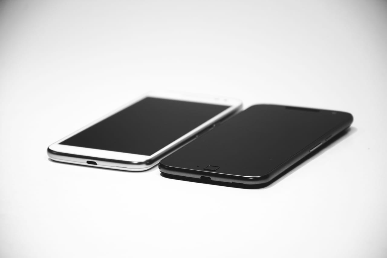 Zwei Smartphones, ein weißes und ein schwarzes, liegen dicht nebeneinander auf hellem Grund