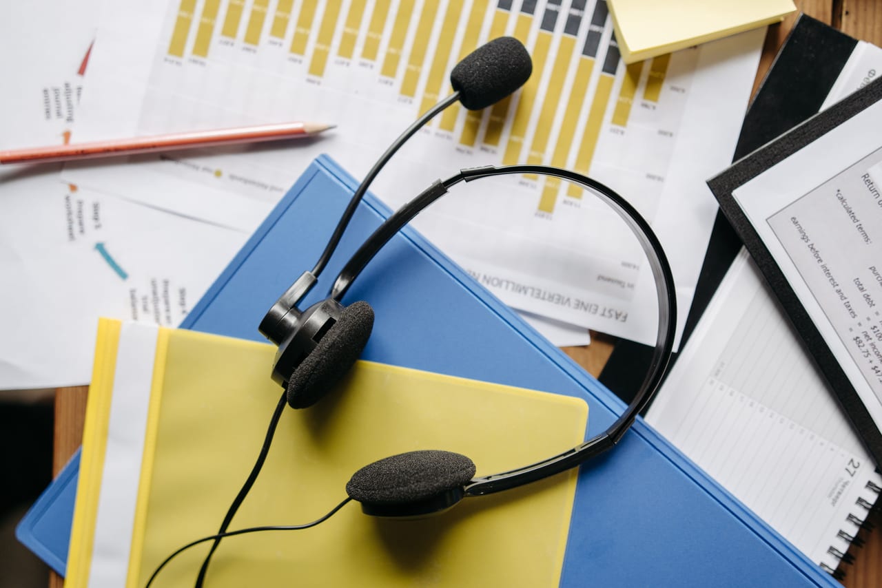 Headset mit Mikrofon liegt auf Ordnern und Unterlagen mit Diagrammen auf einem Schreibtisch