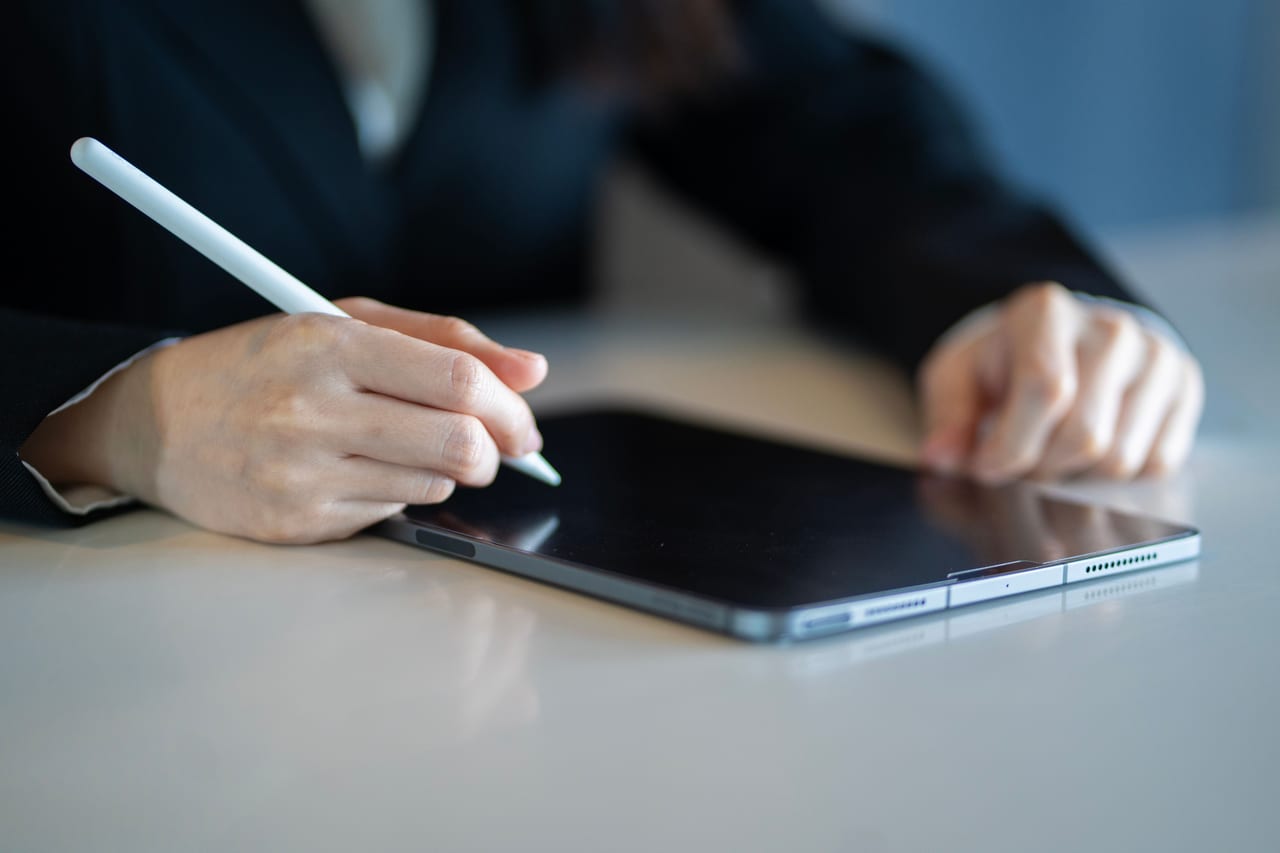 Hände im dunklen Anzug halten einen Eingabestift über ein Tablet