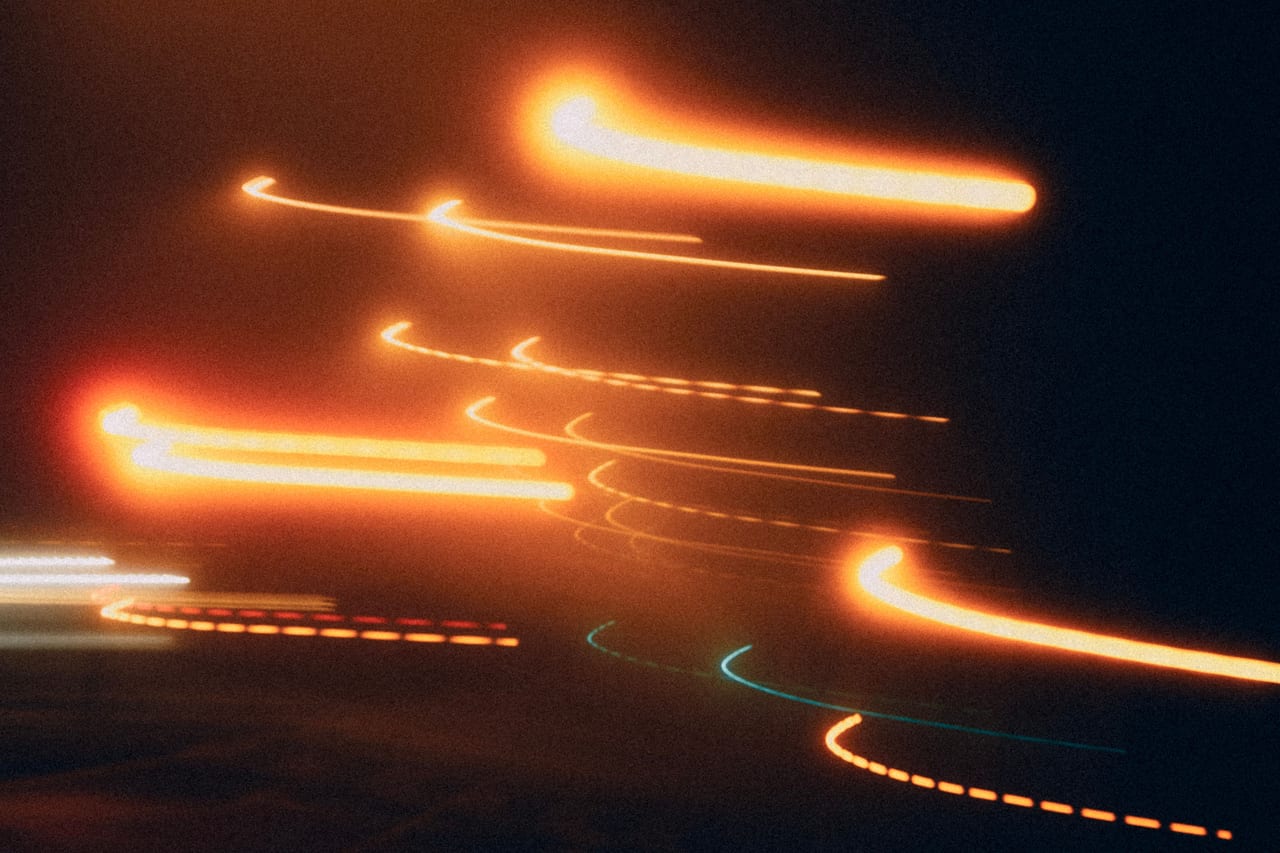 Lichtspuren einer Langzeitbelichtung ziehen als orange Bänder durch die Dunkelheit