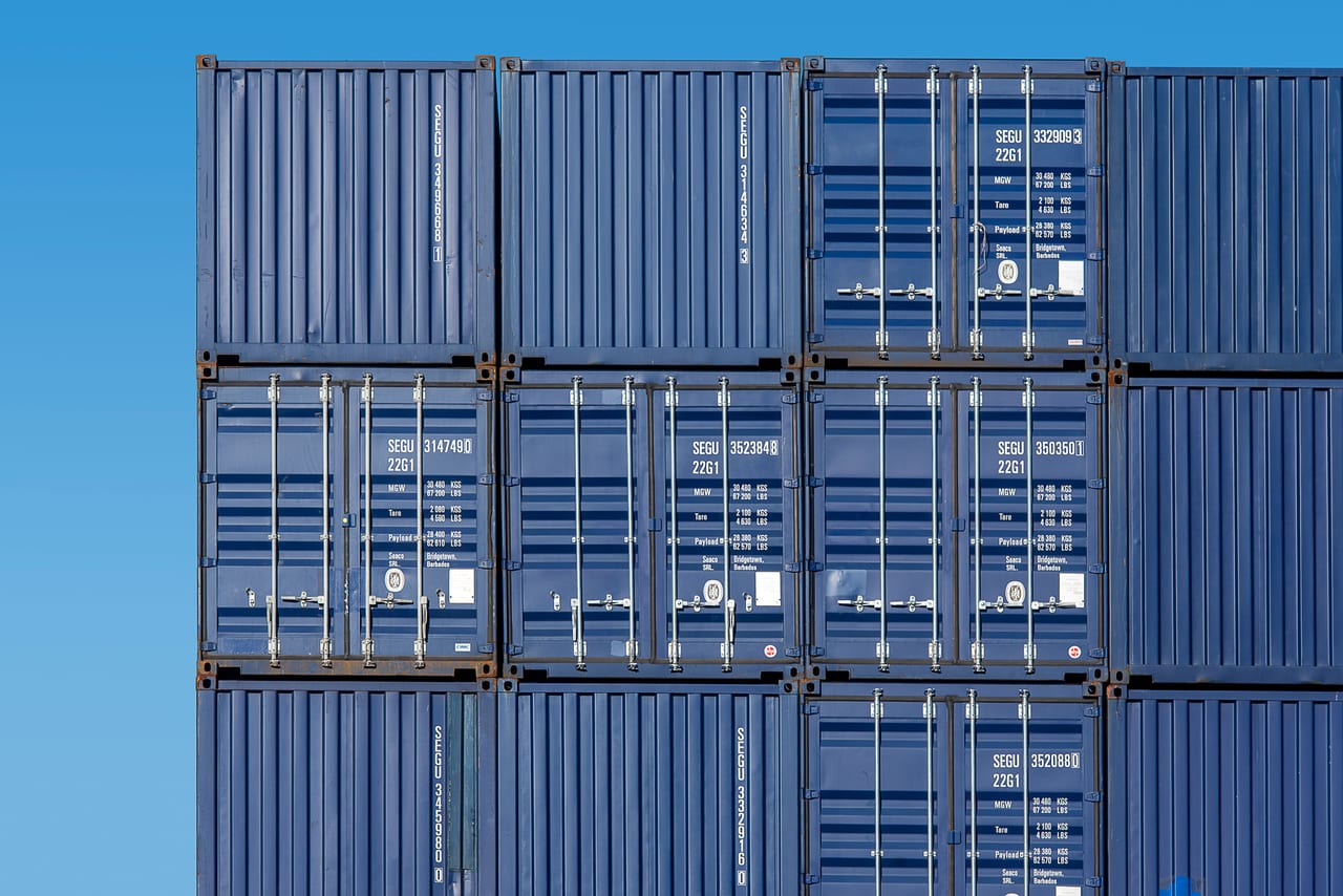 Gestapelte Frachtcontainer in Blau und Grau vor wolkenlosem Himmel