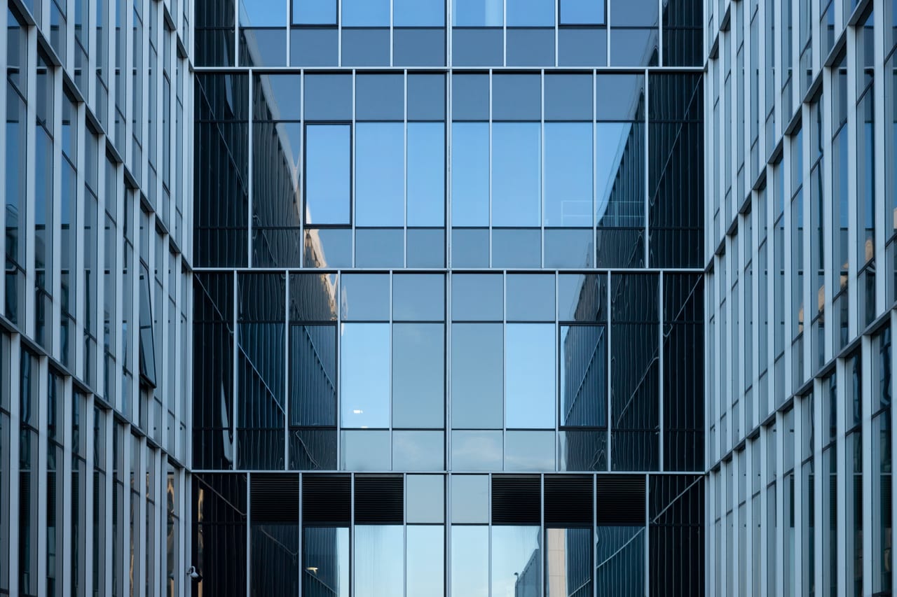 Moderne Bürofassade aus Glas, in den Scheiben spiegeln sich die gegenüberliegenden Gebäude