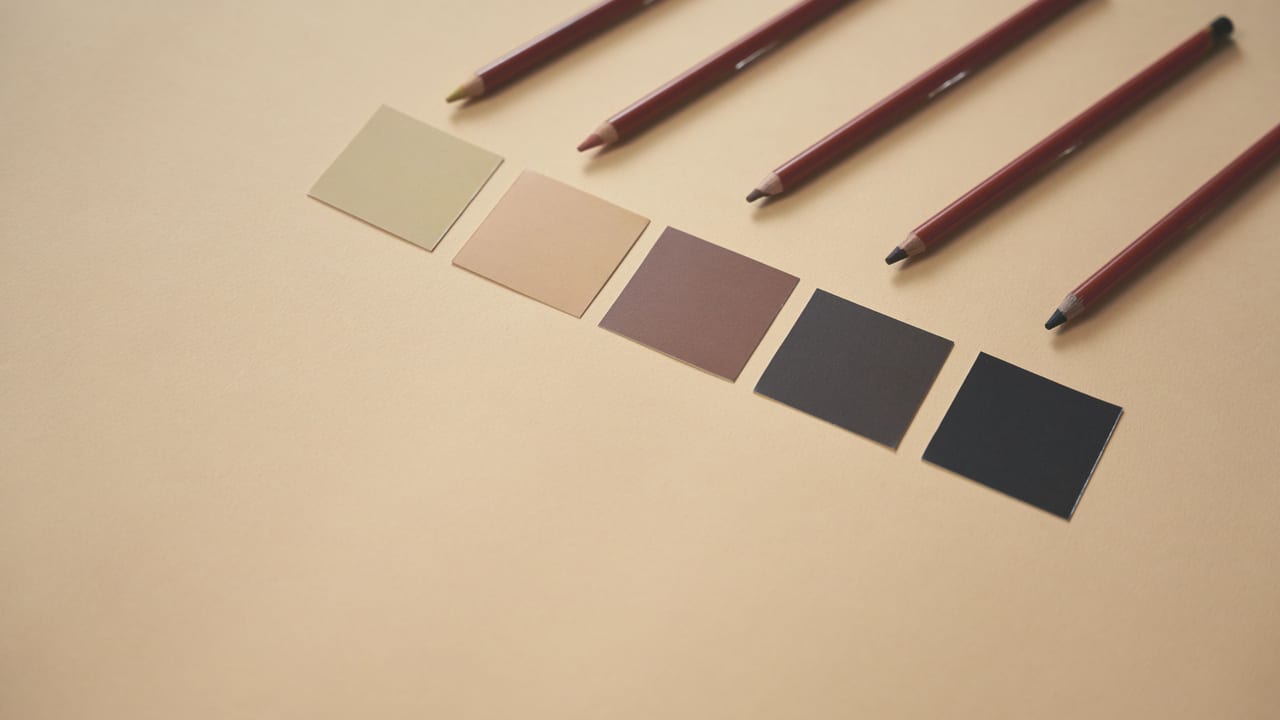 Fünf Farbmuster von Beige bis Anthrazit nebeneinander, daneben angespitzte Buntstifte