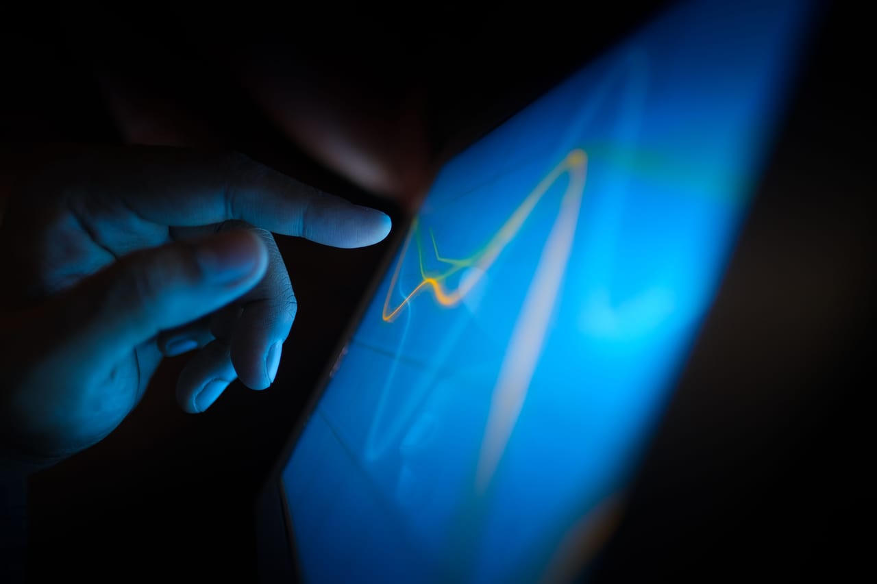 Finger zeigt im blauen Dämmerlicht auf eine leuchtende Verlaufskurve auf einem Tablet
