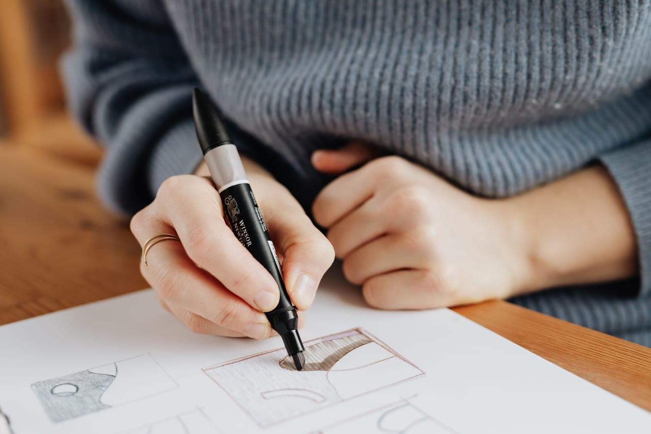Hand zeichnet mit braunem Marker ein Seitenlayout aus Kästen und Spalten auf ein großes Blatt