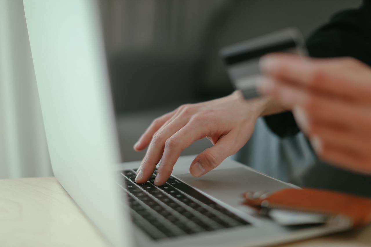 Hände an einer Laptoptastatur, eine Hand hält dabei eine Bankkarte für eine Onlinezahlung
