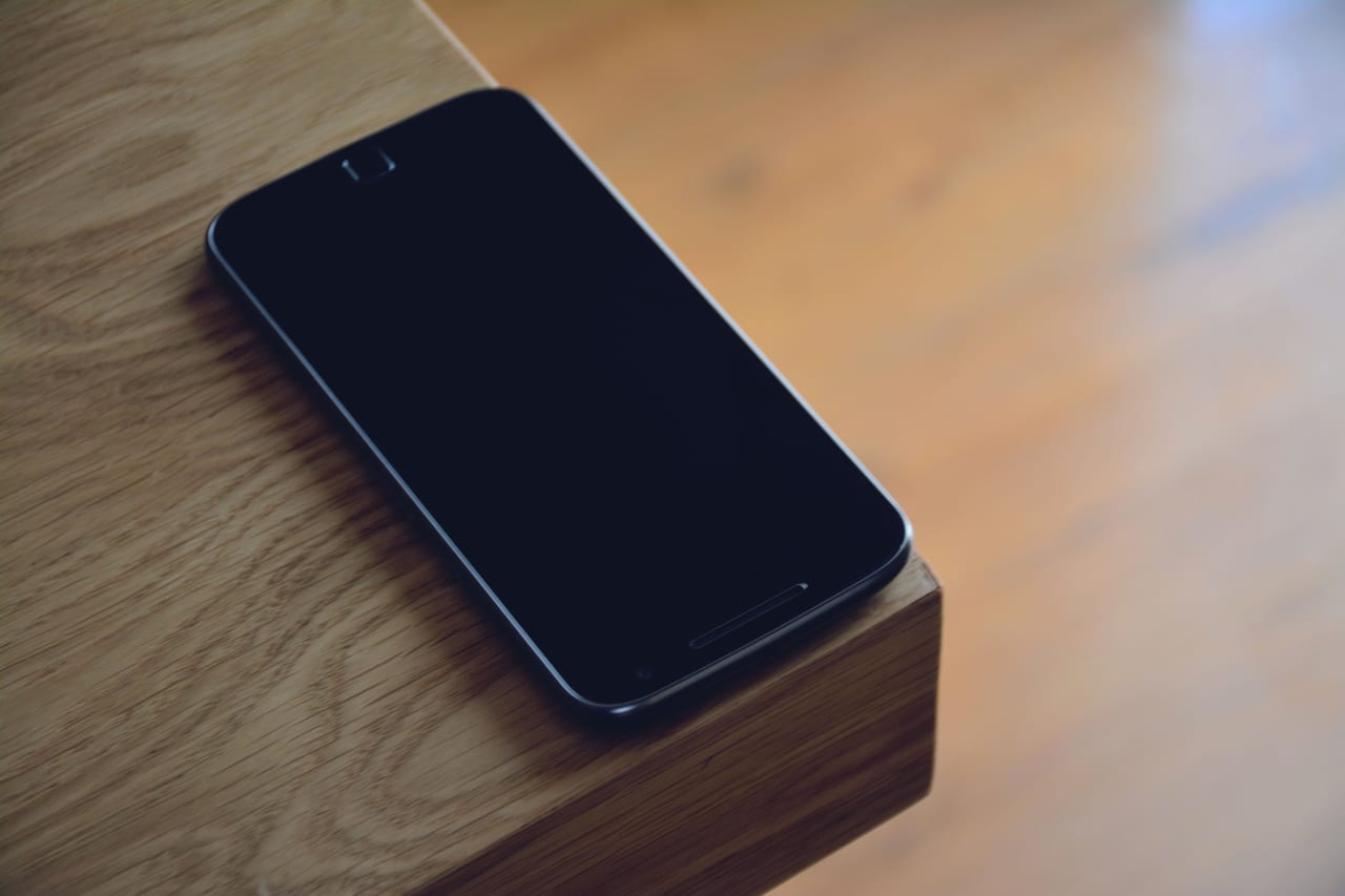 Smartphone mit dunklem Bildschirm liegt an der Kante eines Holztisches