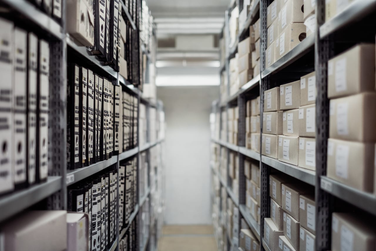 Gang zwischen Metallregalen voller beschrifteter Archivordner in einem Magazin
