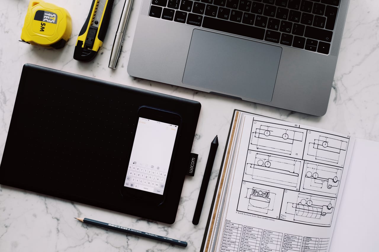Arbeitsplatz von oben mit Grafiktablett, Smartphone, Notebook und Entwurfszeichnungen