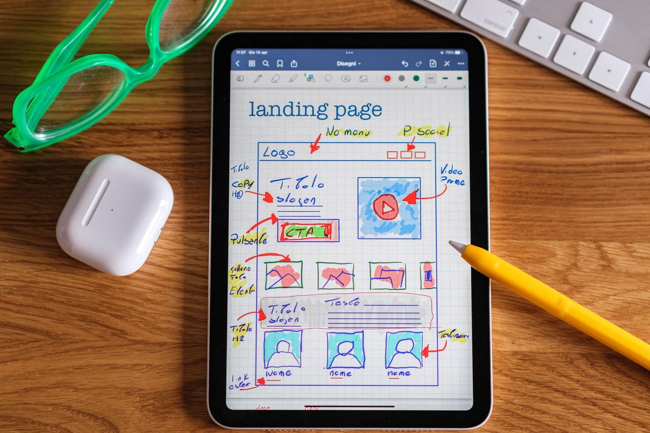 Tablet mit handgezeichnetem Wireframe einer Landingpage mit Logo, Call-to-Action und Bildraster, daneben ein gelber Eingabestift