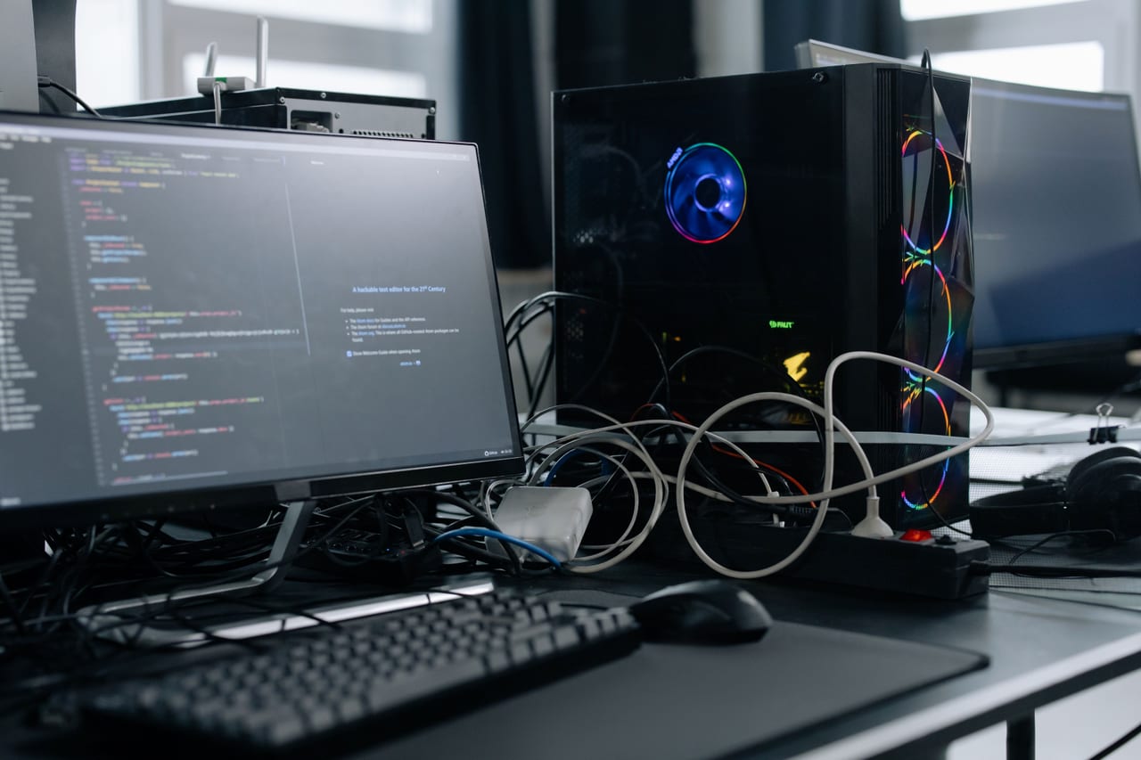 Arbeitsplatz mit zwei Bildschirmen, Tastatur und offenem Rechnergehäuse mit sichtbaren Kabeln