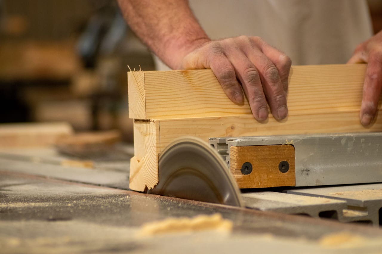 Zwei Hände schieben eine Holzlatte über das Sägeblatt einer Tischkreissäge