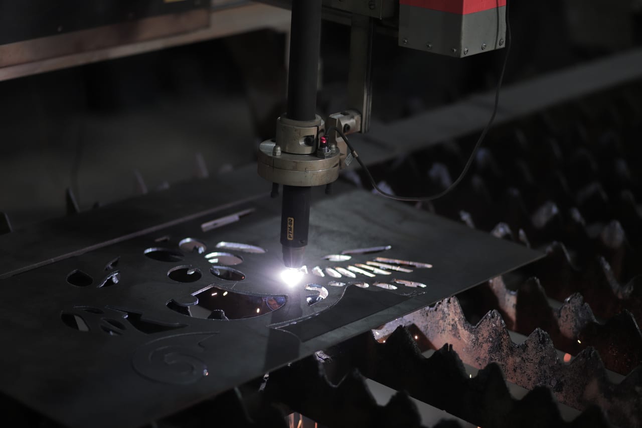 CNC-Plasmaschneider trennt Konturen aus einem Stahlblech, darunter das Auflagegitter mit Funkenflug