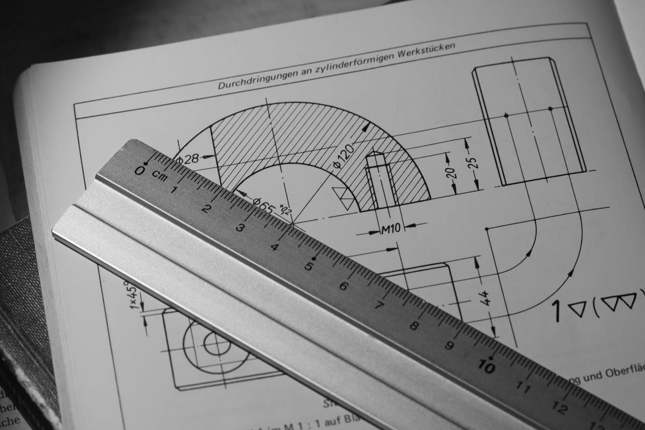 Technische Zeichnung eines zylindrischen Werkstücks mit Bemaßung in einem Fachbuch, darüber ein Stahllineal