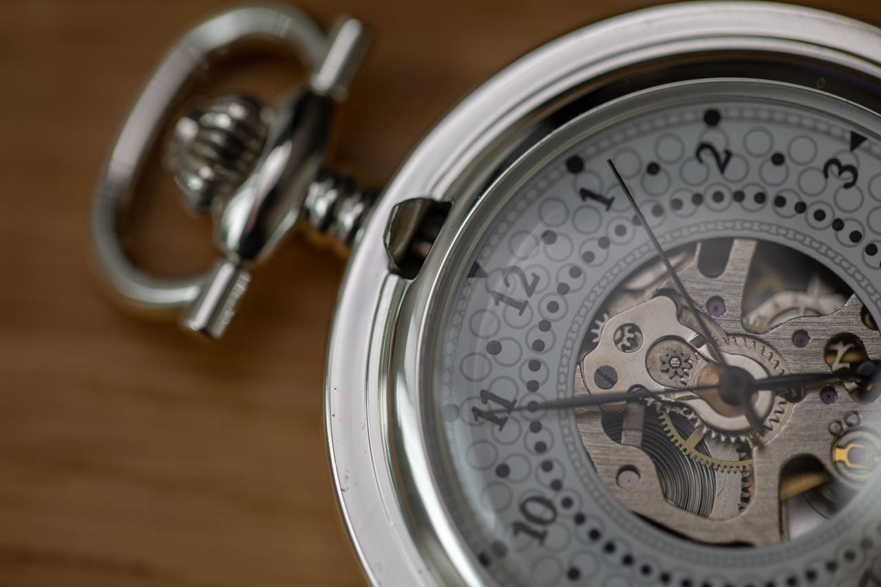 Nahaufnahme einer Taschenuhr mit teilweise offenem Zifferblatt, durch das die Zahnräder des Uhrwerks sichtbar sind