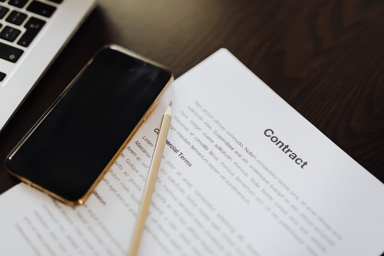 Ausgedruckter Vertrag mit Überschrift und Absätzen, daneben ein Stift und ein Smartphone