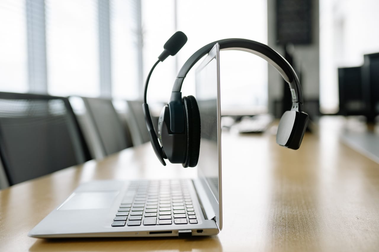 Aufgeklappter Laptop mit drahtlosem Headset auf einem Tisch in einem hellen Büro