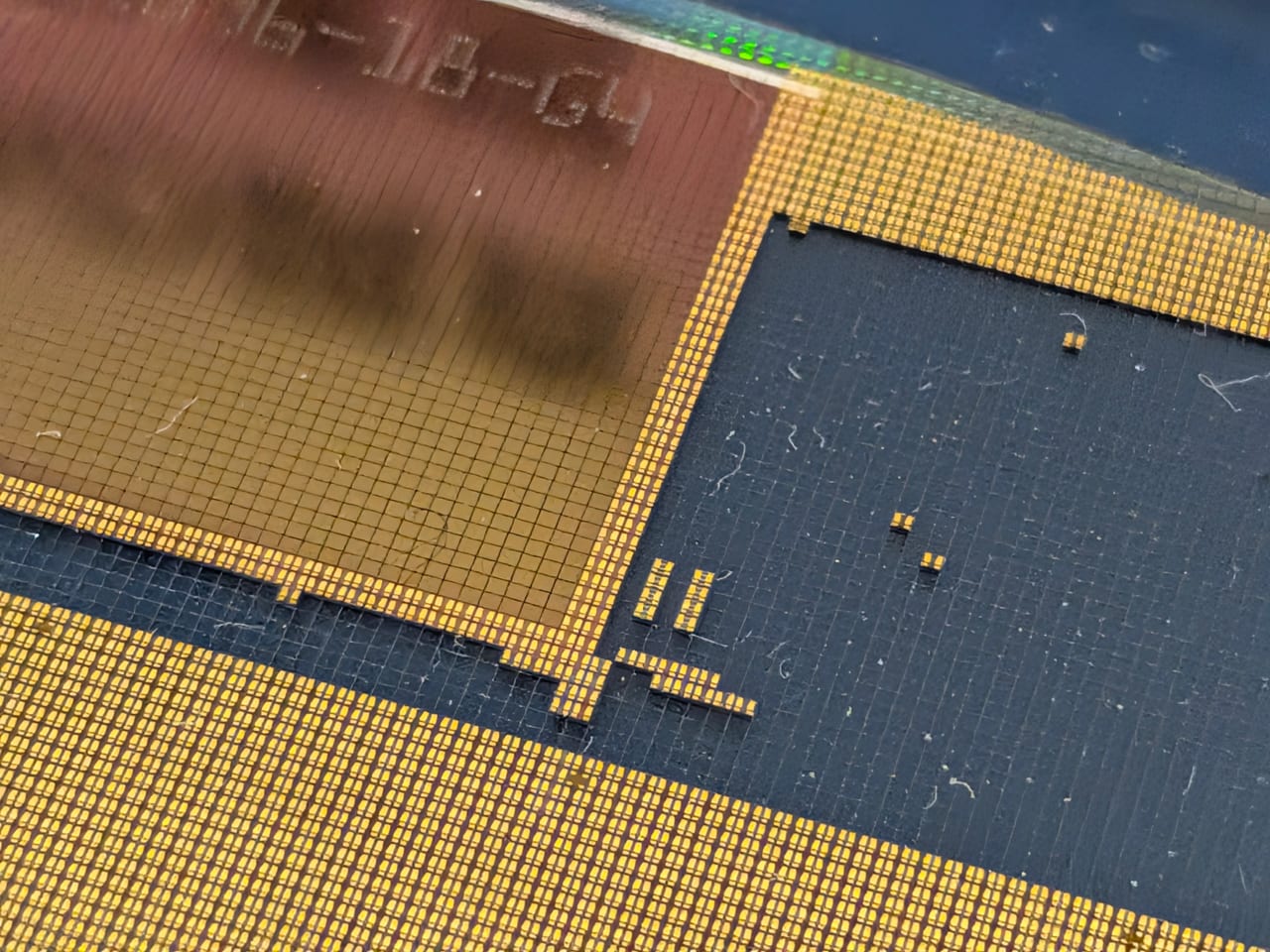 Nahaufnahme winziger goldfarbener Mikrochips in dichten Reihen auf einer blauen Trägerfolie